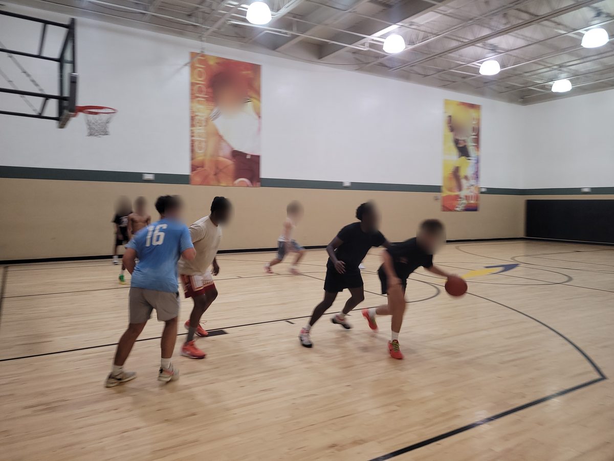 Young guys playing high-energy pickup basketball on an indoor gym court in Hollywood FL, faces blurred