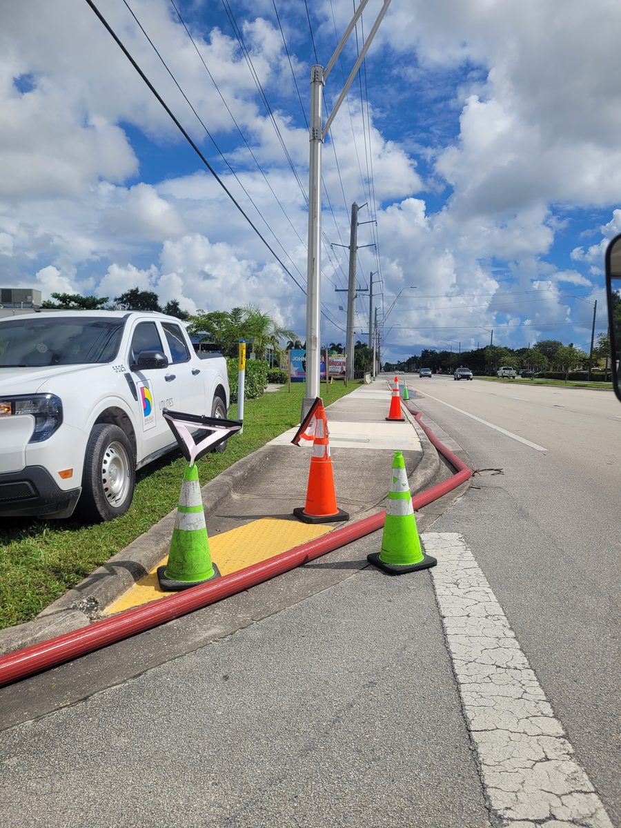 Utility truck and red pump hose along a Dania Beach roadway clearing king tide flood water